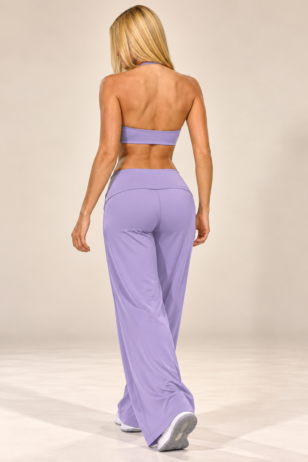 Women's soft lilac activewear outfit with a sleeveless sculpted top and relaxed flared pants, styled with white trainers outside a luxury residence.