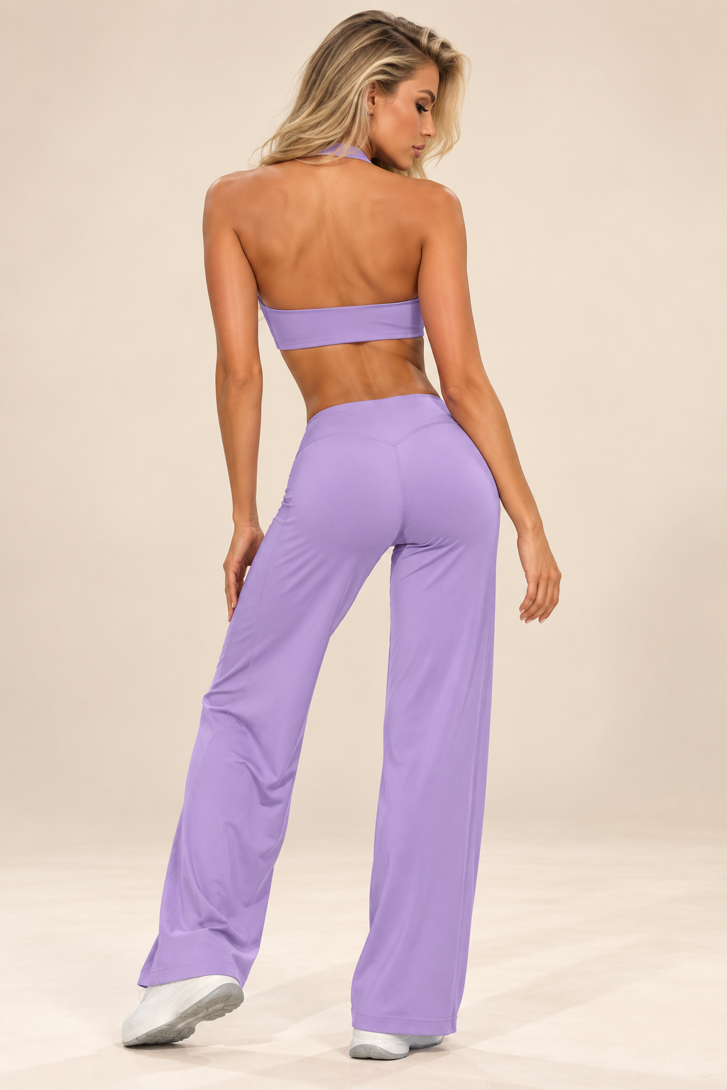 Women's soft lilac activewear outfit with a sleeveless sculpted top and relaxed flared pants, styled with white trainers outside a luxury residence.