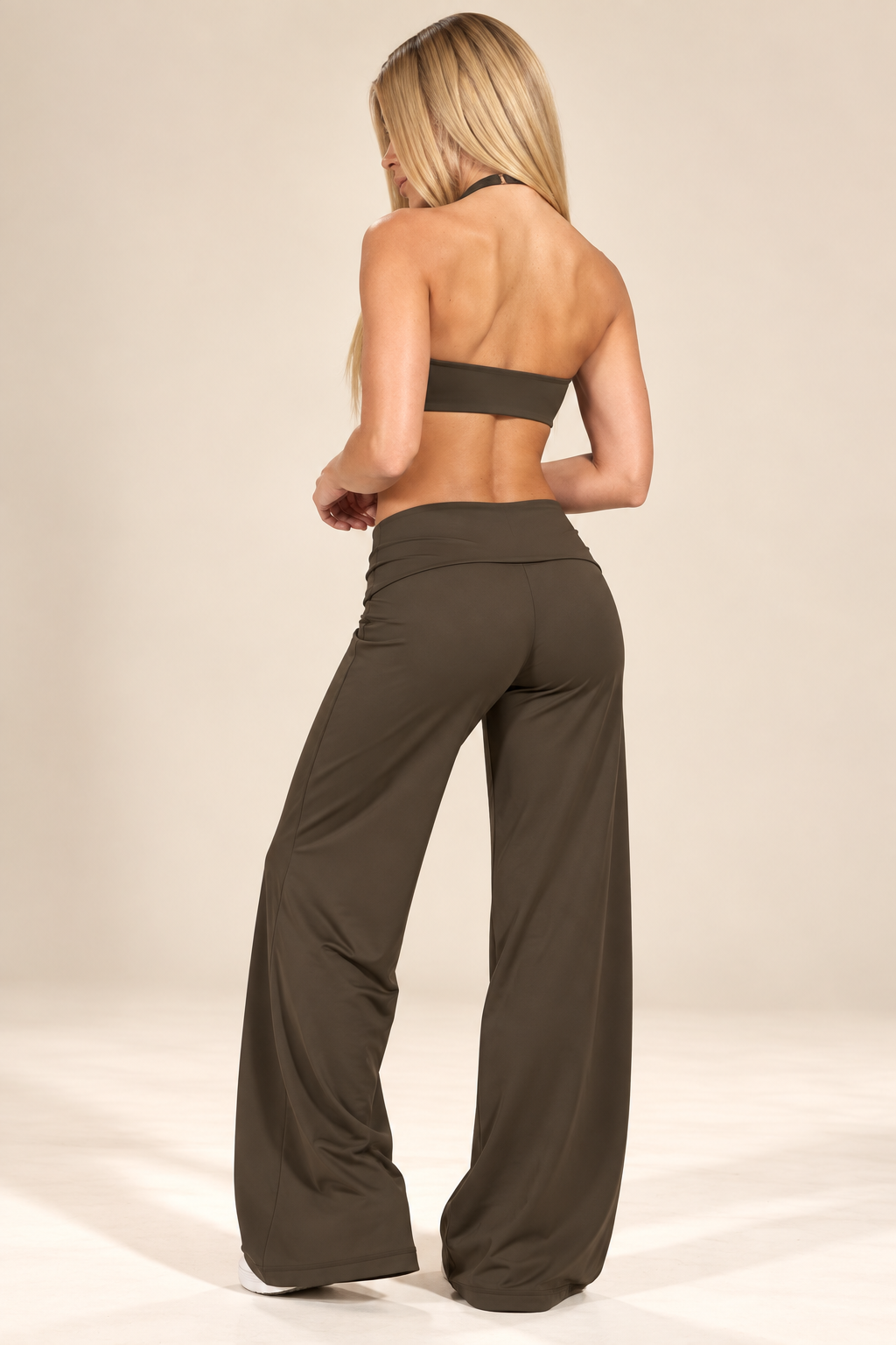 Espresso brown women's golf activewear set with a fitted V-neck crop top and high-waisted wide-leg trousers, photographed beside a golf bag.
