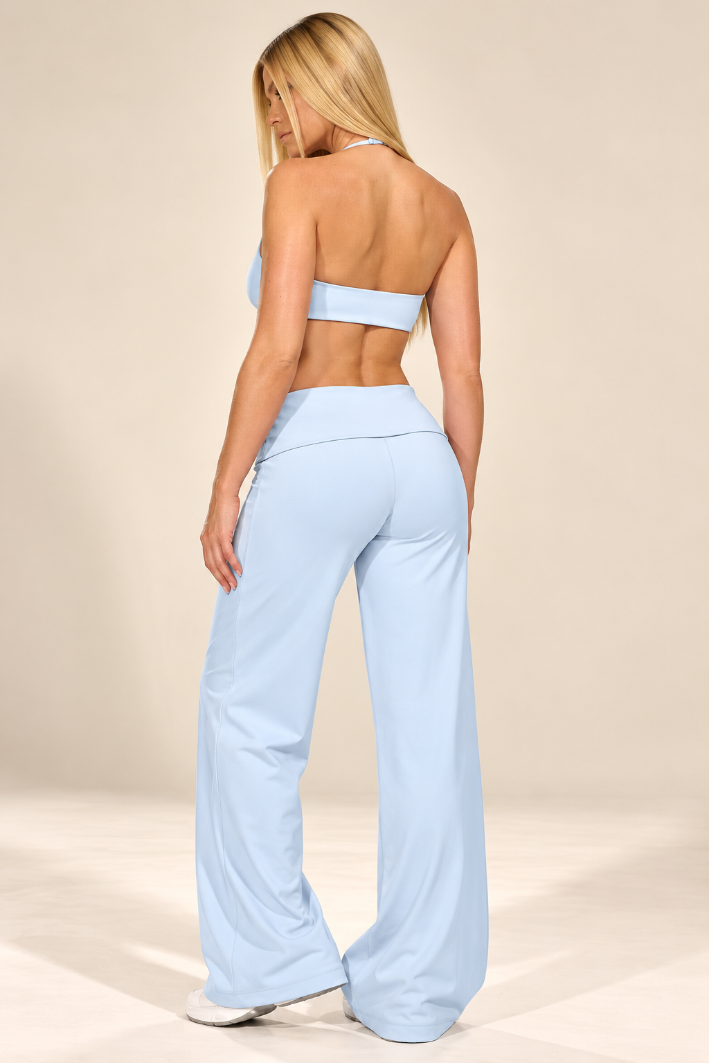 Full-length front view of a light blue two-piece sports set with a cropped halter top and relaxed wide-leg trousers, paired with white trainers.