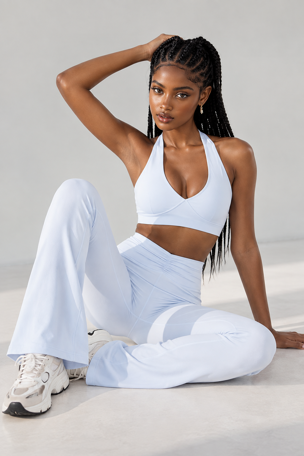 Elegant blue women's yoga set featuring a fitted halter sports top, wide gathered waistband and gently flared athletic leggings, styled with chunky white trainers.