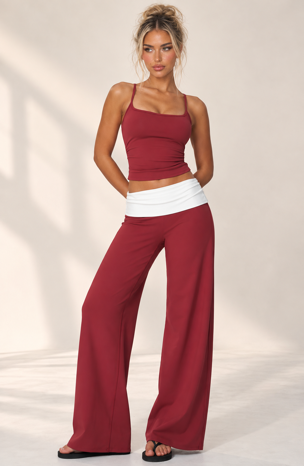 Deep cranberry women’s luxury workout ensemble featuring a high collar zip-up crop jacket, sculpting sports bra and contrast-band wide leg pants