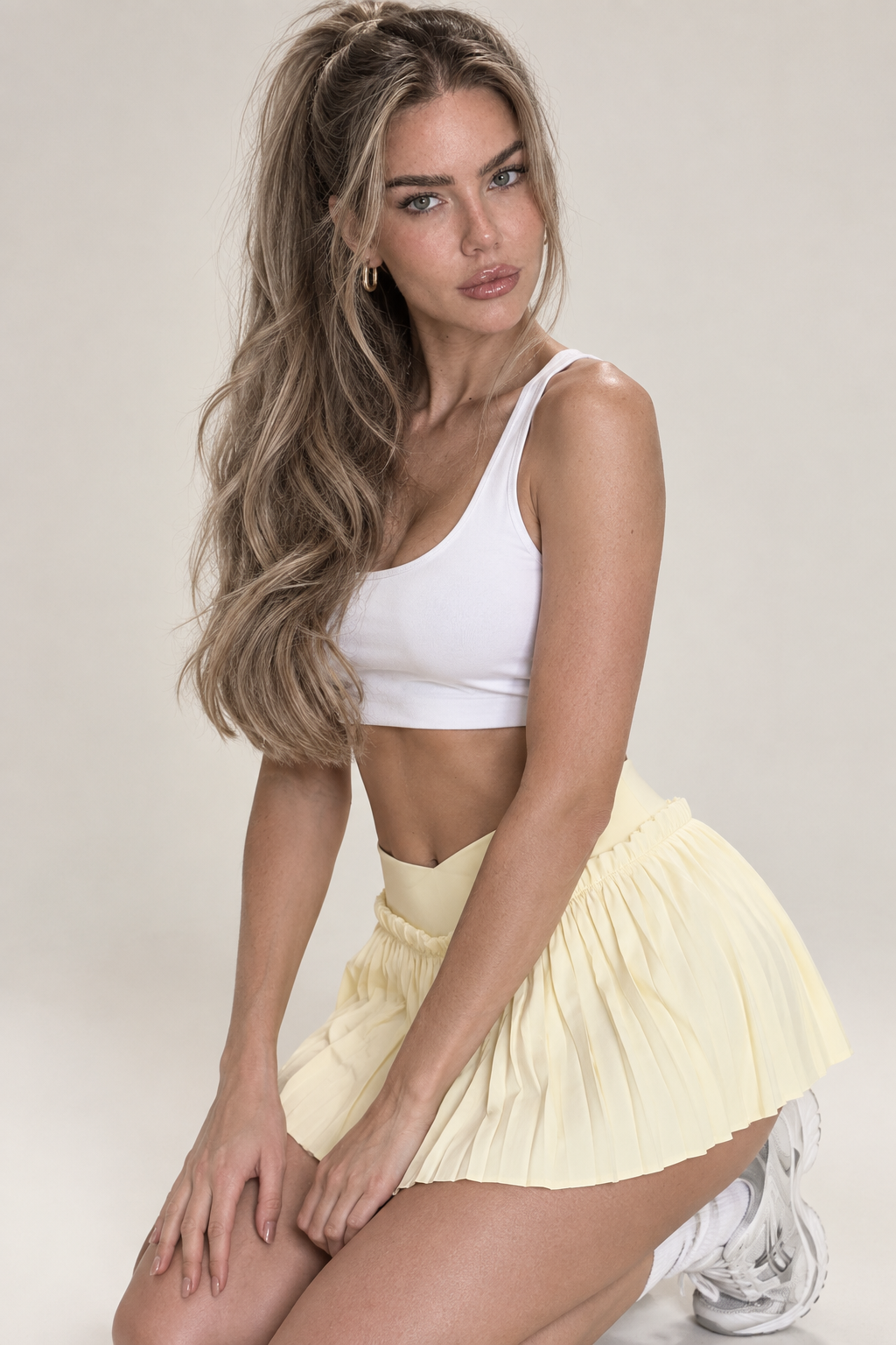 Light vanilla yellow women's tennis two-piece combining a white twist-detail sports bra with a subtle front opening and a feminine high-rise pleated mini skort.