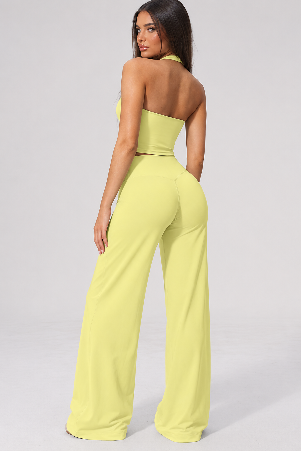 Lime yellow women’s gym wear co ord featuring a scoop halter neck fitted training top and high waisted flowing wide leg workout trousers, combining feminine activewear styling with a relaxed athletic silhouette