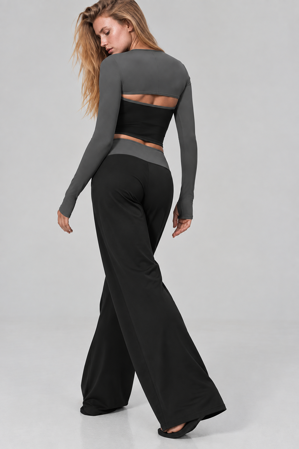 Women’s black and dark grey activewear set featuring layered long sleeves, fitted crop top and contrast waistband wide leg Pilates pants
